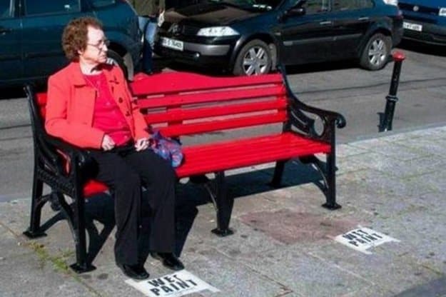 anciana sentada en un banco recién pintado